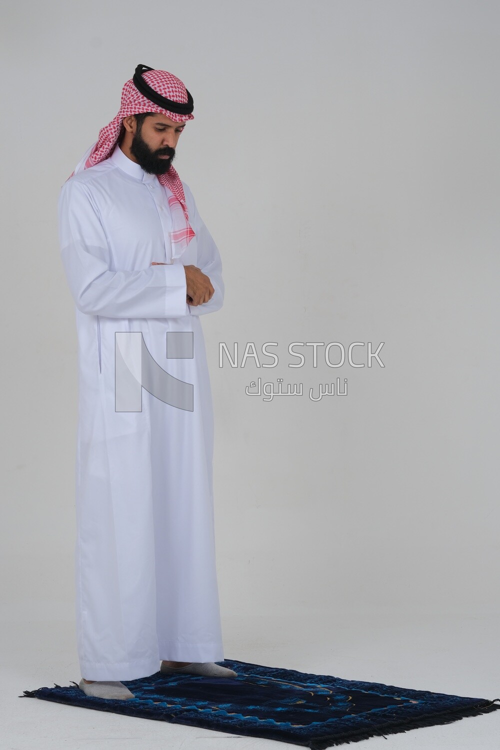 Side view of a Saudi man wearing a white dress sitting on the prayer rug, praying to god, praying on the prayer rug, Islam and worship, white background, Saudi model