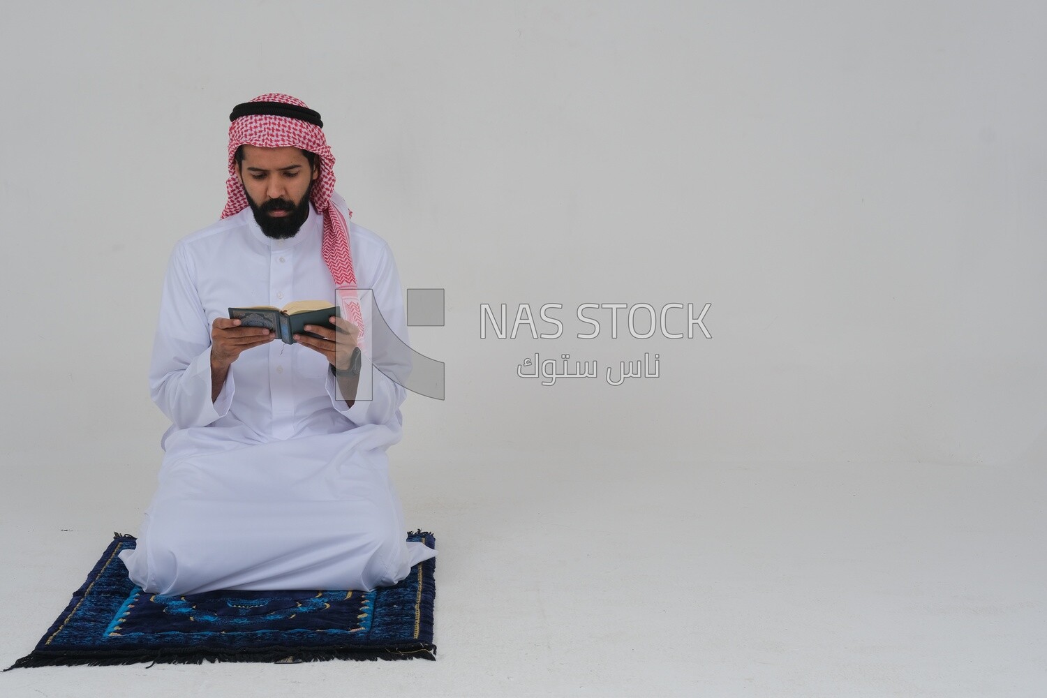 Saudi man wearing a white dress sitting on the prayer rug, reading the Quran, praying to god, praying at the prayer rug, Islam and worship, white background, Saudi model