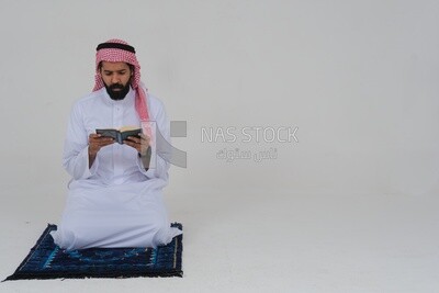 Saudi man wearing a white dress sitting on the prayer rug, reading the Quran, praying to god, praying at the prayer rug, Islam and worship, white background, Saudi model