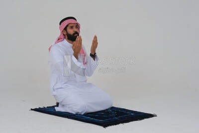 منظر جانبى لرجل سعودي يرتدي ثوبا أبيض يجلس على سجادة الصلاة ، يدعو الله ، يصلي على سجادة الصلاة ، الإسلام والعبادة ، خلفية بيضاء ، موديل سعودي