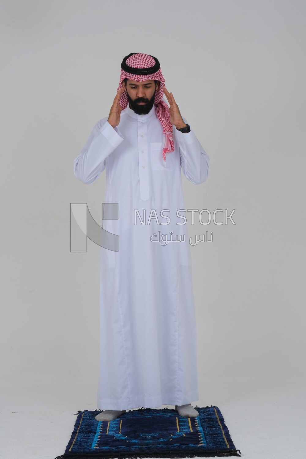 Saudi man wearing a white thobe and shemagh praying on the prayer rug, praying to god, Islam and worship, white background, Saudi model