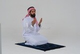 Saudi man wearing a white dress sitting on the prayer rug, praying to god, praying on the prayer rug, Islam and worship, white background, Saudi model