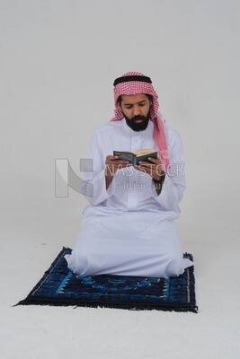 رجل سعودي يرتدي ثوبا أبيض يجلس على السجادة ، يقرا قران ، يصلى الى الله ، يصلي على السجادة ،  الاسلام والعبادة ،  خلفية بيضاء ، موديل سعودي
