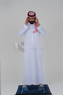 Saudi man wearing a white dress sitting on the prayer rug, praying to god, praying on the prayer rug, Islam and worship, white background, Saudi model