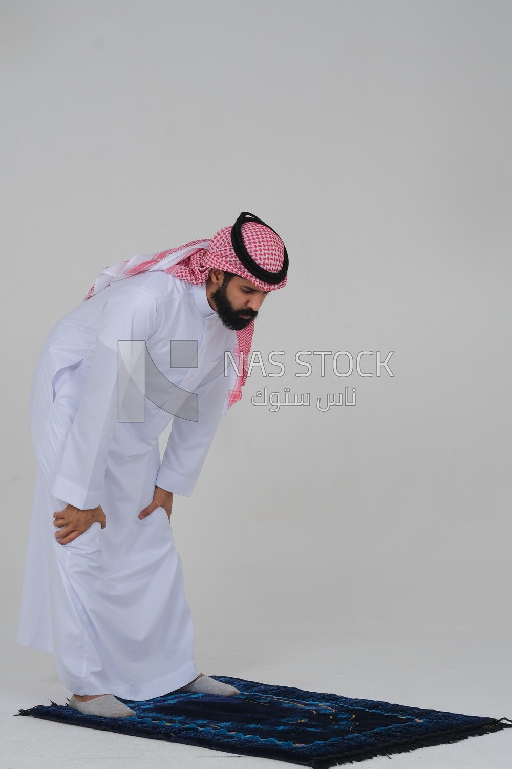 Side view of a Saudi man wearing a white dress sitting on the prayer rug, praying to god, praying on the prayer rug, Islam and worship, white background, Saudi model