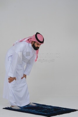 Side view of a Saudi man wearing a white dress sitting on the prayer rug, praying to god, praying on the prayer rug, Islam and worship, white background, Saudi model