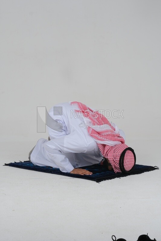 Side view of a Saudi man wearing a white dress sitting on the prayer rug, praying to god, praying on the prayer rug, Islam and worship, white background, Saudi model