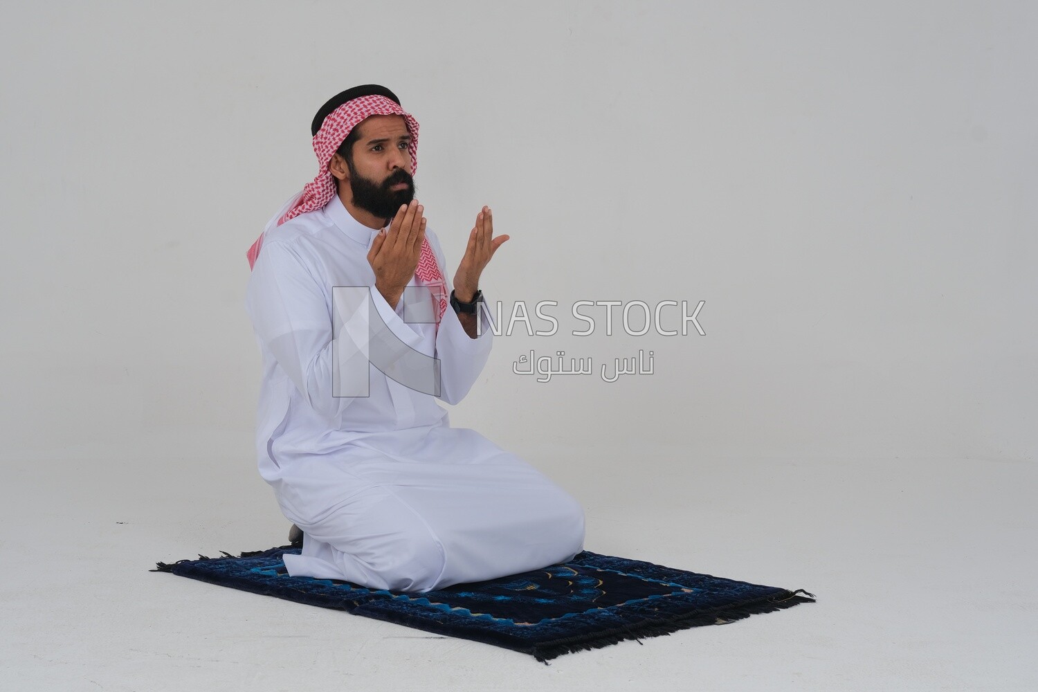 Saudi man wearing a white thobe and shemagh praying on the prayer rug, praying to god, Islam and worship, white background, Saudi model