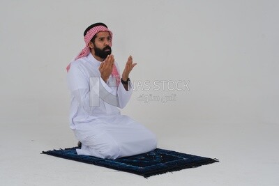 Saudi man wearing a white thobe and shemagh praying on the prayer rug, praying to god, Islam and worship, white background, Saudi model