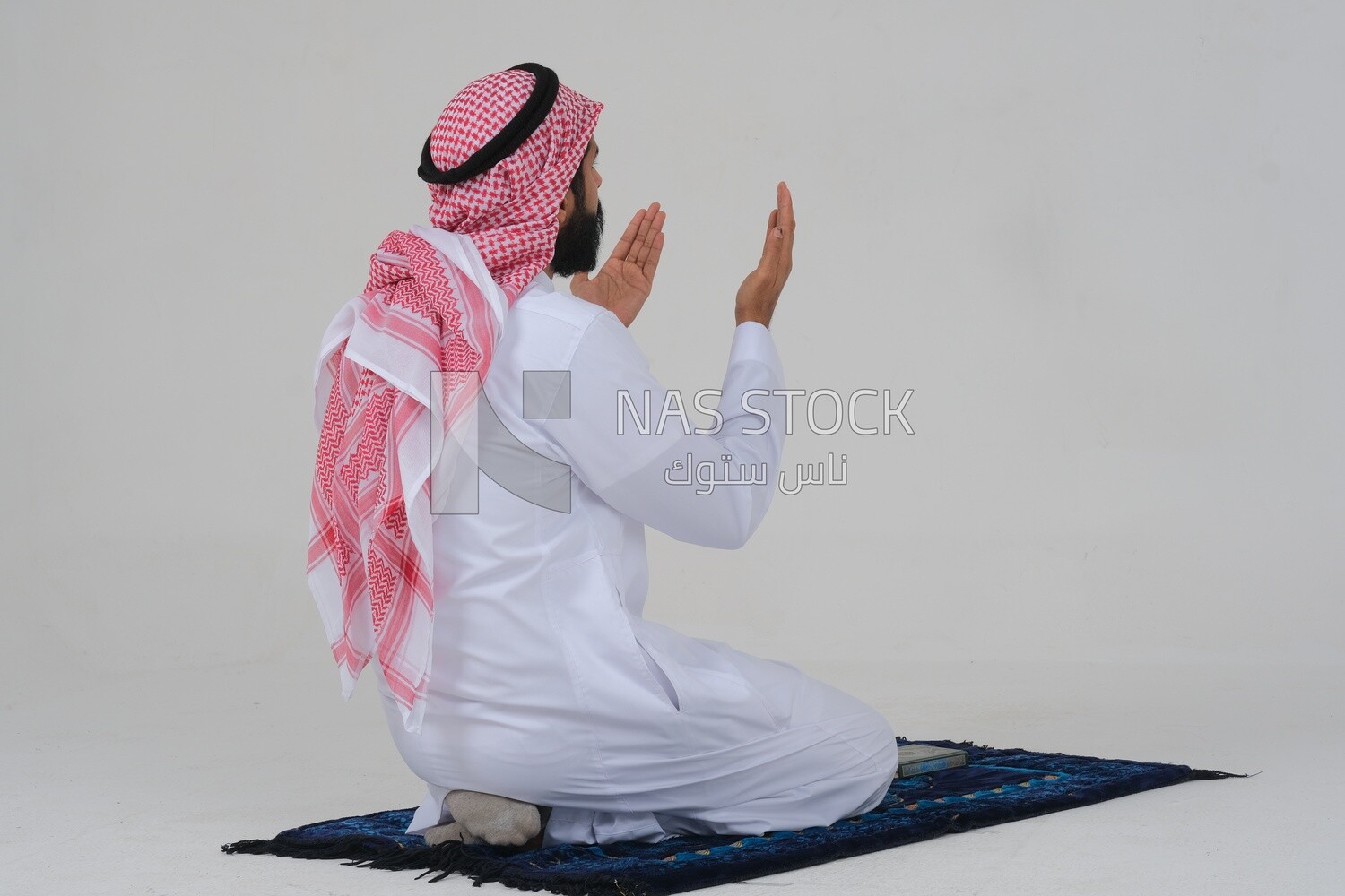 Back of a Saudi man wearing a white dress sitting on the prayer rug, praying to god, praying on the prayer rug, Islam and worship, white background, Saudi model