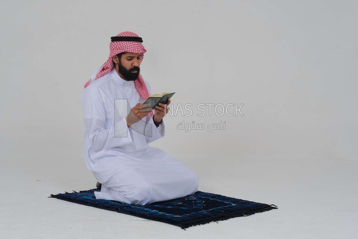 Saudi man wearing a white dress sitting on a chair, reading Quran, Islam and worship, Saudi model, white background