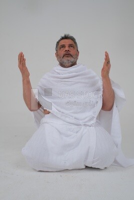 Saudi man wearing the Ihram dress and raising his hands to supplicate to God, Islam and worship, performing Hajj and Umrah, remembrances and supplications, white background, Saudi model