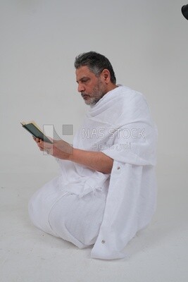 Saudi man wearing the Ihram dress and holding the Holy Quran book, praying to god, Islam and worship, performing Hajj and Umrah, remembrances and supplications, white background, Saudi model