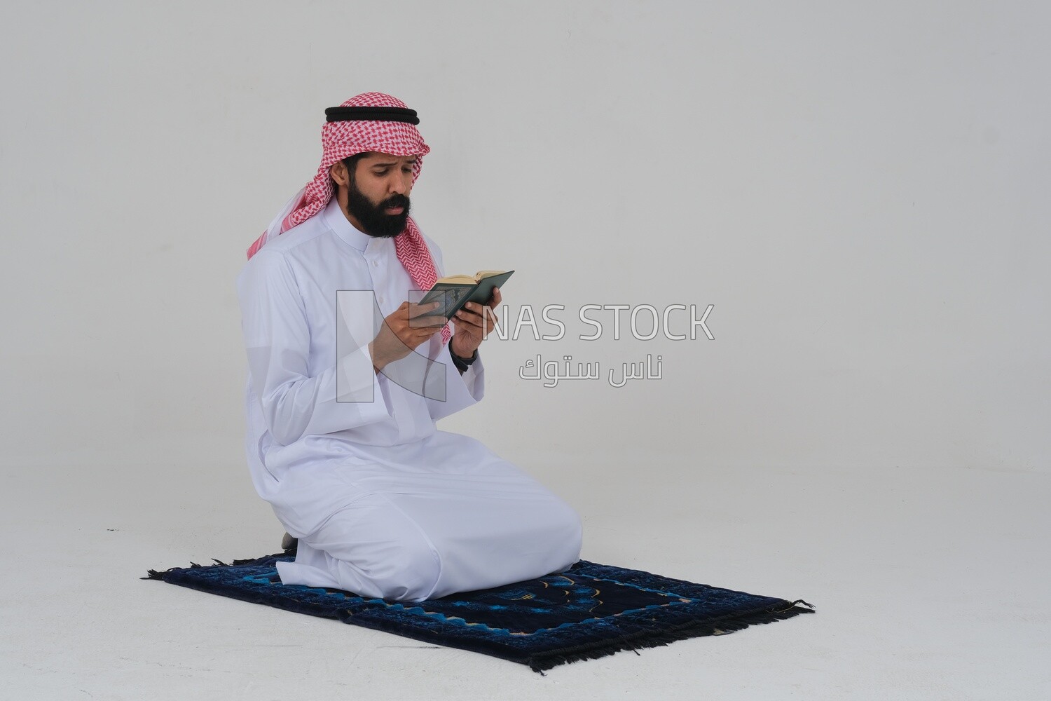 Saudi man wearing a white dress sitting on the prayer rug, reading the Quran, praying to god, praying at the prayer rug, Islam and worship, white background, Saudi model