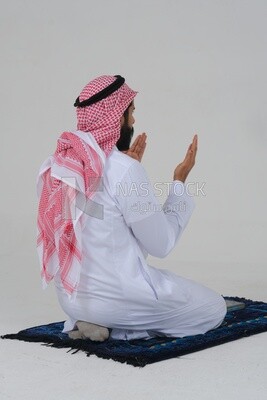Back of a Saudi man wearing a white dress sitting on the prayer rug, praying to god, praying on the prayer rug, Islam and worship, white background, Saudi model