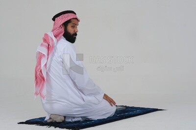 Back of a Saudi man wearing a white dress sitting on the prayer rug, praying to god, praying on the prayer rug, Islam and worship, white background, Saudi model