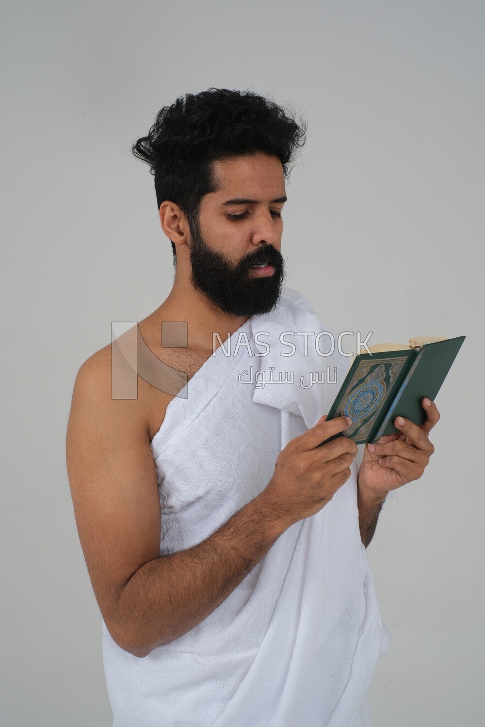 Saudi man wearing the Ihram dress and holding the Holy Quran book, praying to god, Islam and worship, performing Hajj and Umrah, remembrances and supplications, white background, Saudi model