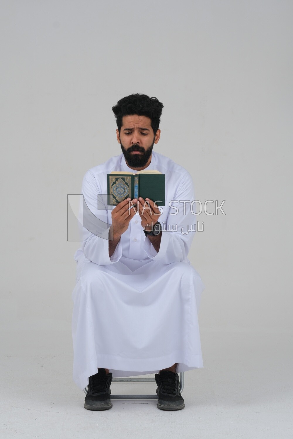 Saudi man wearing a white dress sitting on a chair, reading Quran, Islam and worship, Saudi model, white background