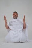 Saudi man wearing the Ihram dress and raising his hands to supplicate to God, Islam and worship, performing Hajj and Umrah, remembrances and supplications, white background, Saudi model