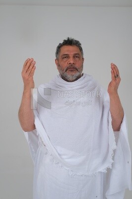 Saudi man wearing the Ihram dress and raising his hands to supplicate to God, Islam and worship, performing Hajj and Umrah, remembrances and supplications, white background, Saudi model