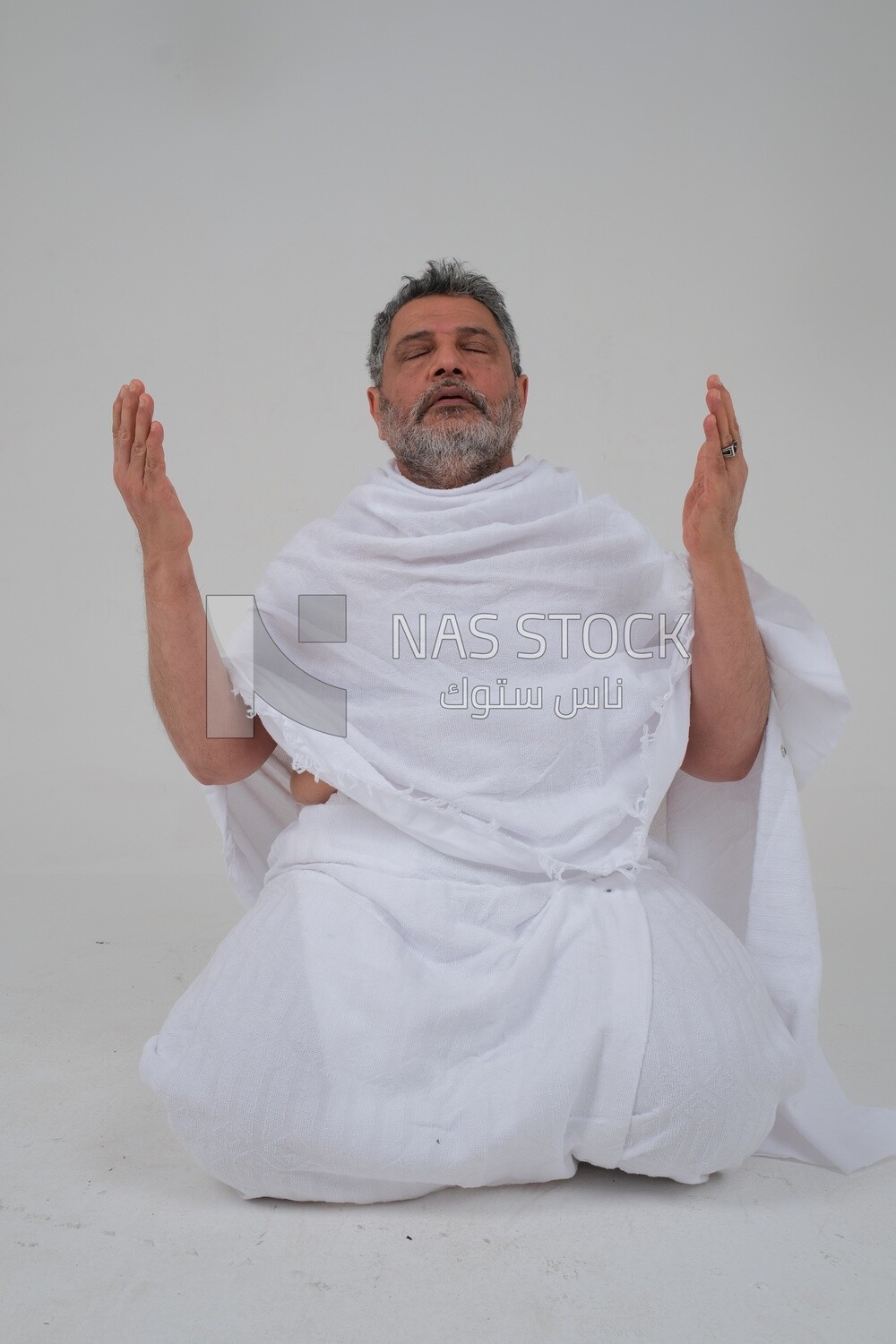 Saudi man wearing the Ihram dress and raising his hands to supplicate to God, Islam and worship, performing Hajj and Umrah, remembrances and supplications, white background, Saudi model