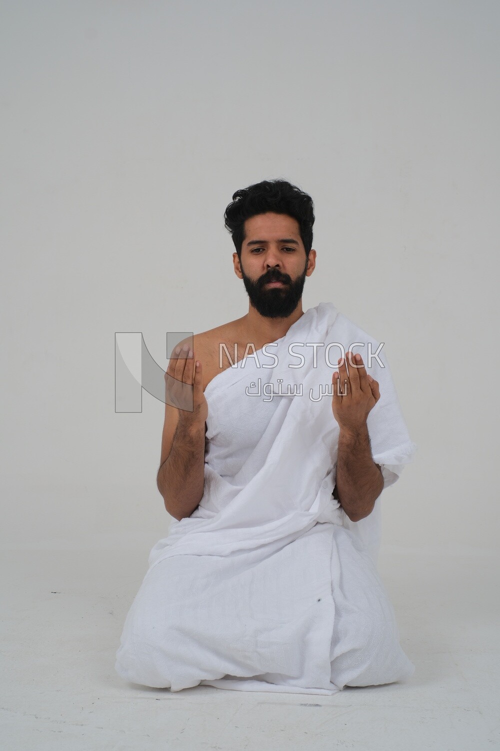 Saudi man wearing the Ihram dress and raising his hands to supplicate to God, Islam and worship, performing Hajj and Umrah, remembrances and supplications, white background, Saudi model