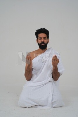 Saudi man wearing the Ihram dress and raising his hands to supplicate to God, Islam and worship, performing Hajj and Umrah, remembrances and supplications, white background, Saudi model