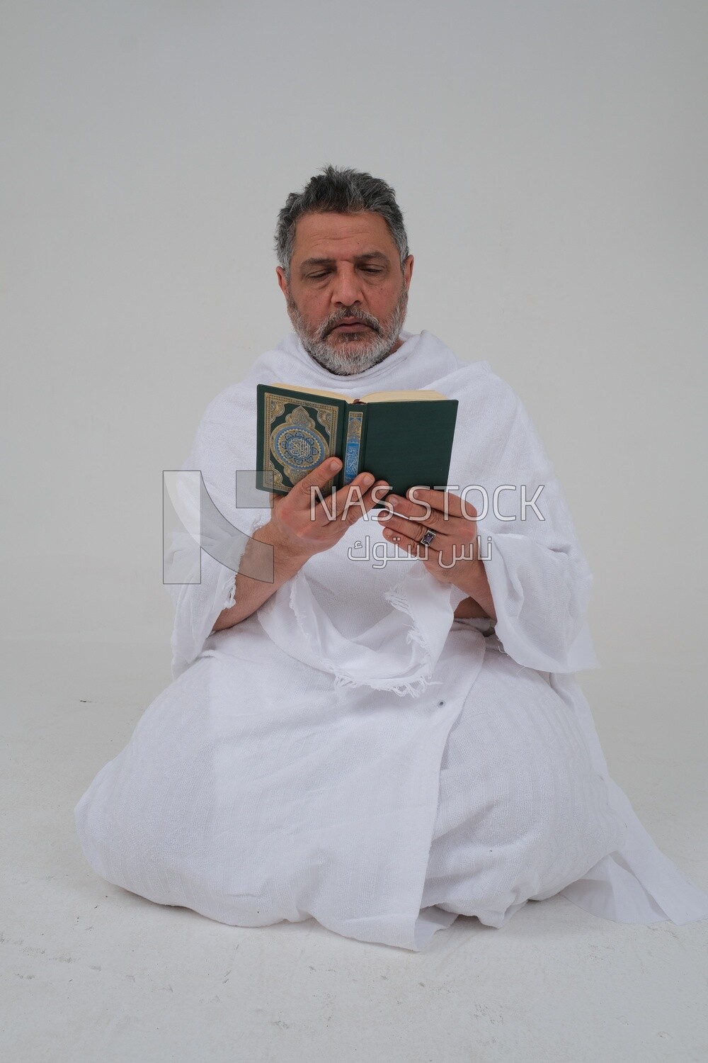 Saudi man wearing the Ihram dress and holding the Holy Quran book, praying to god, Islam and worship, performing Hajj and Umrah, remembrances and supplications, white background, Saudi model