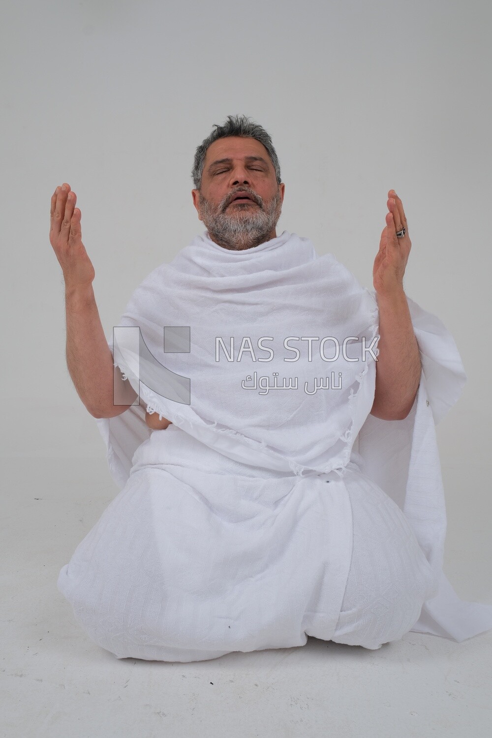 Saudi man wearing the Ihram dress and raising his hands to supplicate to God, Islam and worship, performing Hajj and Umrah, remembrances and supplications, white background, Saudi model