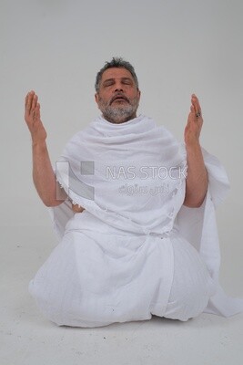 Saudi man wearing the Ihram dress and raising his hands to supplicate to God, Islam and worship, performing Hajj and Umrah, remembrances and supplications, white background, Saudi model