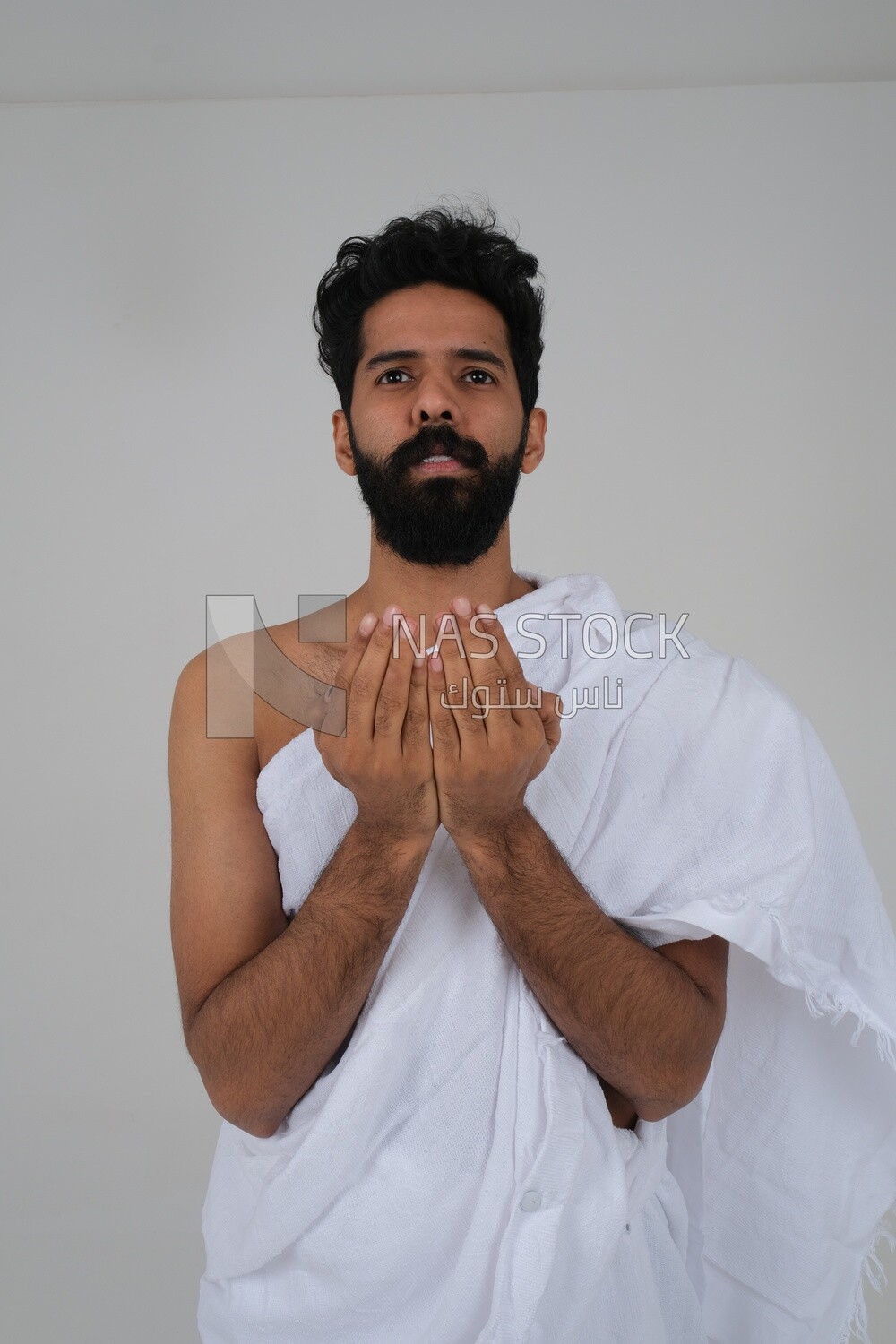 Saudi man wearing the Ihram dress and raising his hands to supplicate to God, Islam and worship, performing Hajj and Umrah, remembrances and supplications, white background, Saudi model