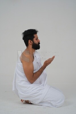 Side of a Saudi man wearing the Ihram dress and raising his hands to supplicate to God, Islam and worship, performing Hajj and Umrah, remembrances and supplications, white background, Saudi model