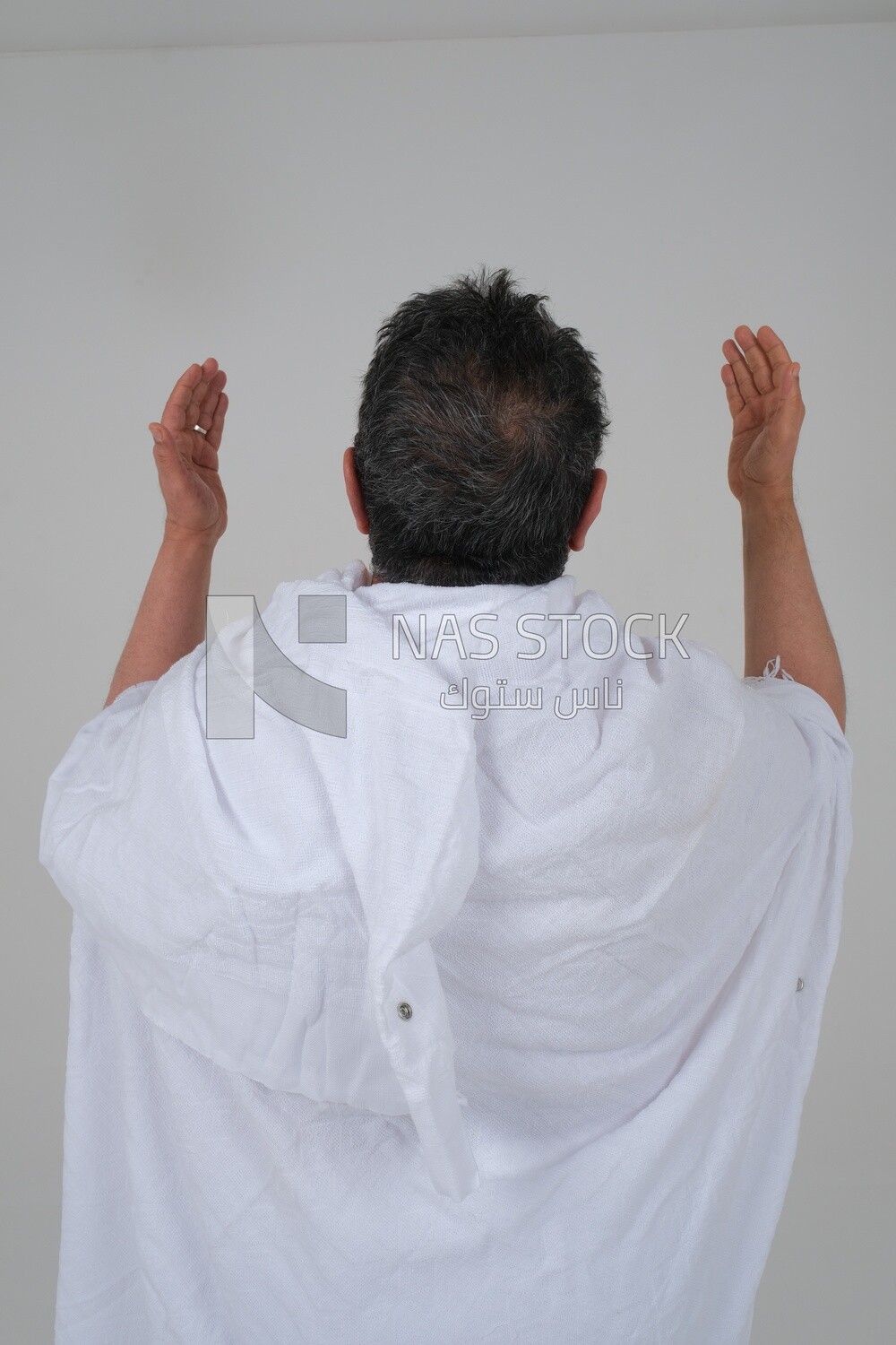 Back of a Saudi man wearing the Ihram dress and raising his hands to supplicate to God, Islam and worship, performing Hajj and Umrah, remembrances and supplications, white background, Saudi model