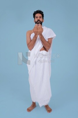 Saudi man wearing the Ihram dress and raising his hands to supplicate to God, Islam and worship, performing Hajj and Umrah, remembrances and supplications, Saudi model