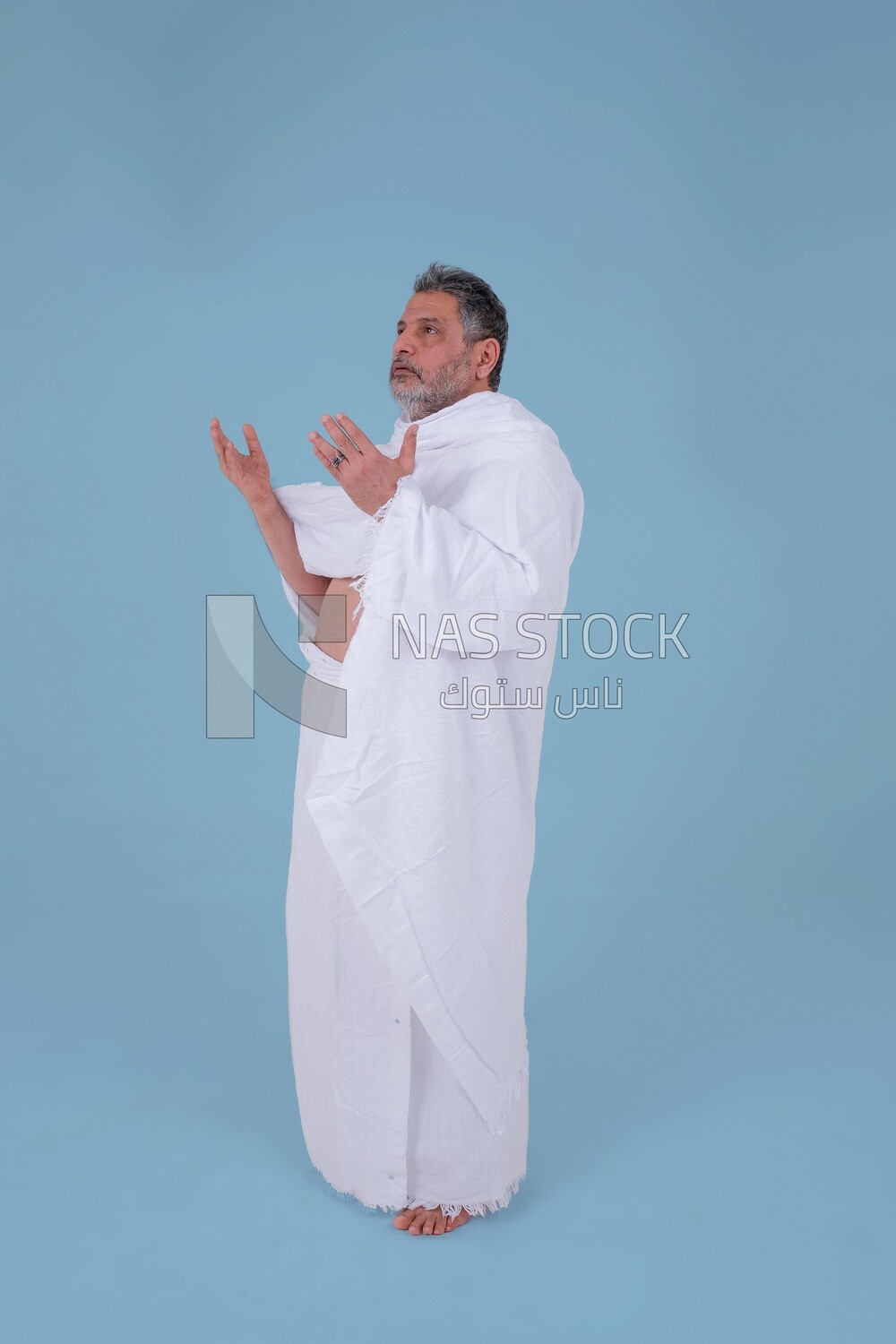 Side of a Saudi man wearing the Ihram dress and raising his hands to supplicate to God, Islam and worship, performing Hajj and Umrah, remembrances and supplications, Saudi model