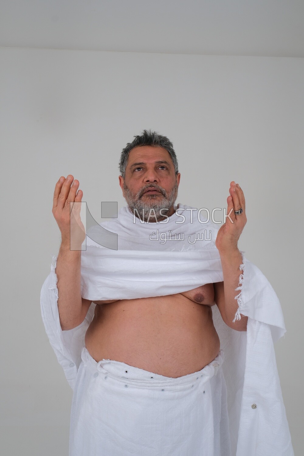 Saudi man wearing the Ihram dress and raising his hands to supplicate to God, Islam and worship, performing Hajj and Umrah, remembrances and supplications, white background, Saudi model