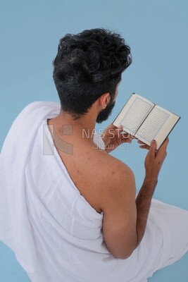 Back of a Saudi man wearing the Ihram dress and holding the Holy Quran book, praying to god, Islam and worship, performing Hajj and Umrah, remembrances and supplications, Saudi model