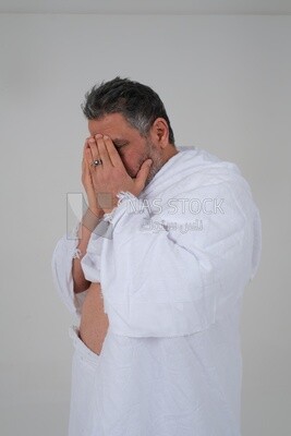 Saudi man wearing the Ihram dress puts his hand on his face to supplicate to God, Islam and worship, performing Hajj and Umrah, remembrances and supplications, white background, Saudi model