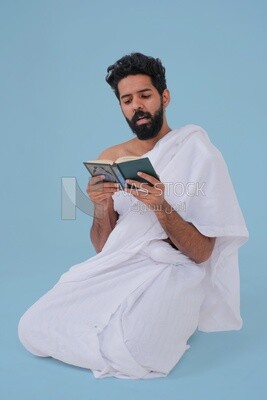 Saudi man wearing the Ihram dress and holding the Holy Quran book, praying to god, Islam and worship, performing Hajj and Umrah, remembrances and supplications, Saudi model