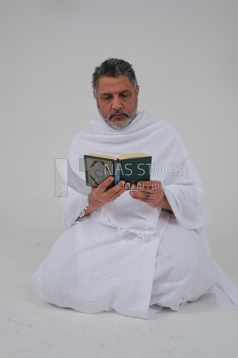 Saudi man wearing the Ihram dress and holding the Holy Quran book, praying to god, Islam and worship, performing Hajj and Umrah, remembrances and supplications, white background, Saudi model