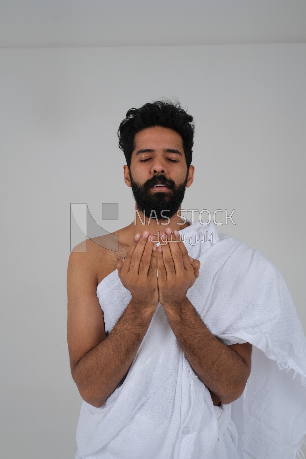 Saudi man wearing the Ihram dress and raising his hands to supplicate to God, Islam and worship, performing Hajj and Umrah, remembrances and supplications, white background, Saudi model