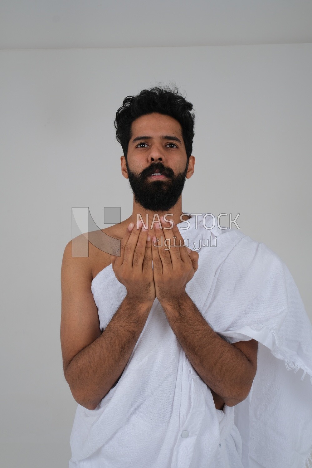 Saudi man wearing the Ihram dress and raising his hands to supplicate to God, Islam and worship, performing Hajj and Umrah, remembrances and supplications, white background, Saudi model