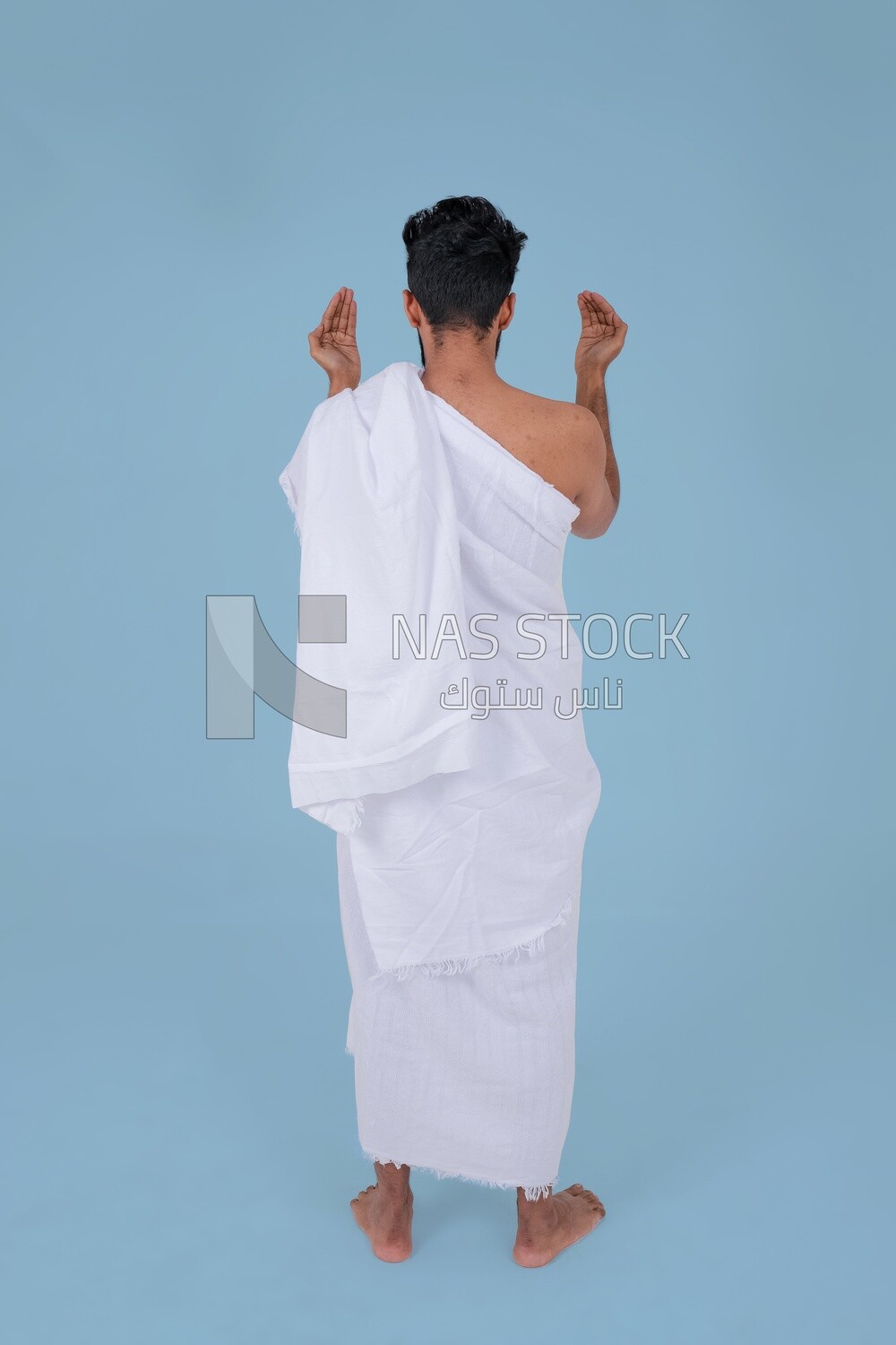 Back of a Saudi man wearing the Ihram dress and raising his hands to supplicate to God, Islam and worship, performing Hajj and Umrah, remembrances and supplications, Saudi model