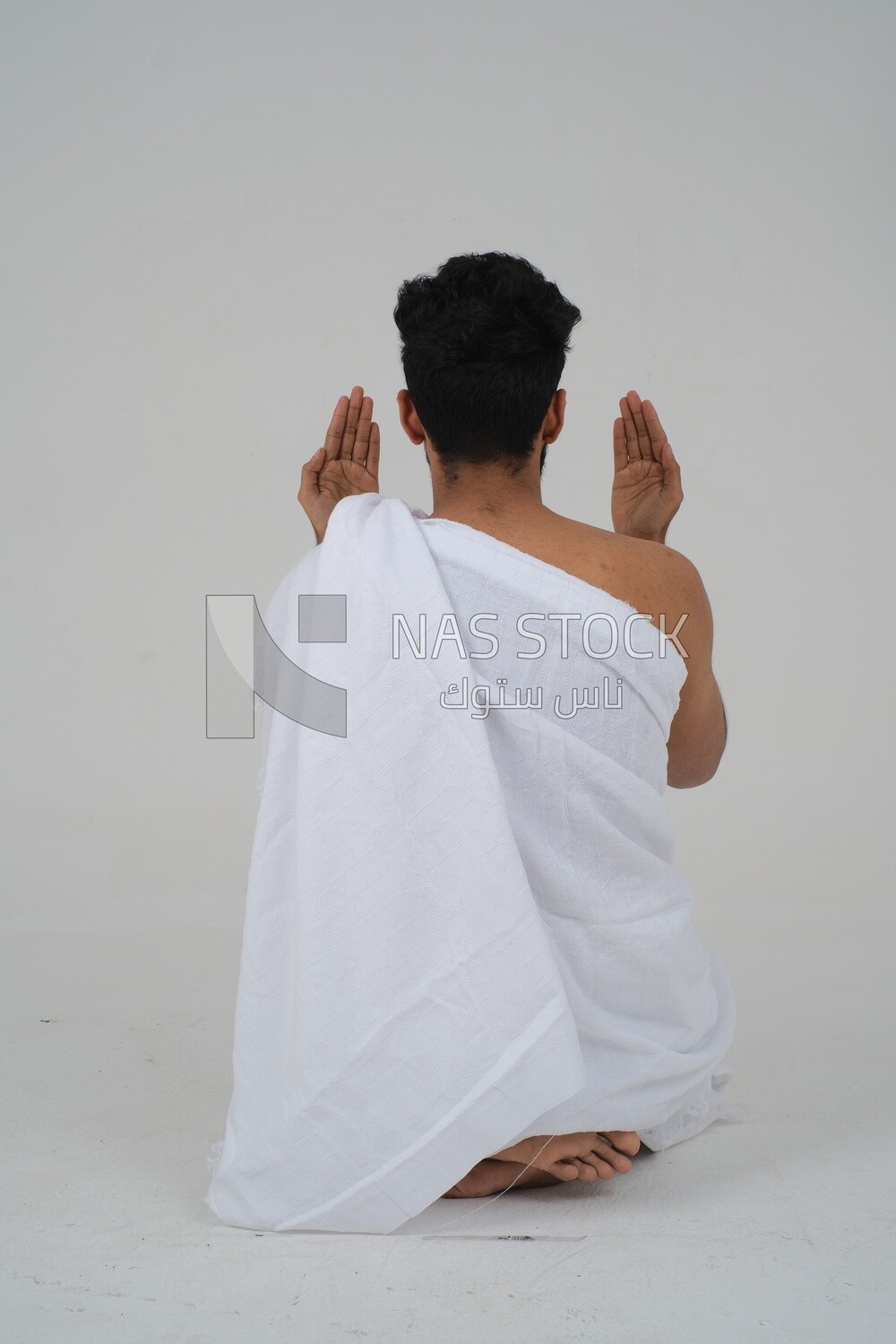 Back of a Saudi man wearing the Ihram dress and raising his hands to supplicate to God, Islam and worship, performing Hajj and Umrah, remembrances and supplications, white background, Saudi model