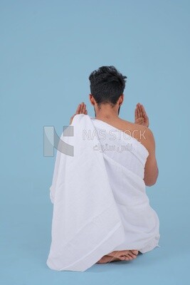 Back of a Saudi man wearing the Ihram dress and raising his hands to supplicate to God