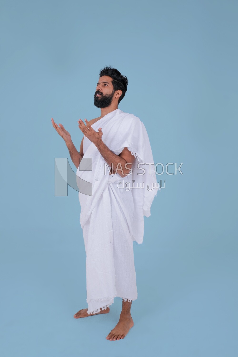 Side of a Saudi man wearing the Ihram dress and raising his hands to supplicate to God, Islam and worship, performing Hajj and Umrah, remembrances and supplications, Saudi model