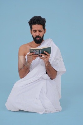 Saudi man wearing the Ihram dress and holding the Holy Quran book, praying to god, Islam and worship, performing Hajj and Umrah, remembrances and supplications, Saudi model