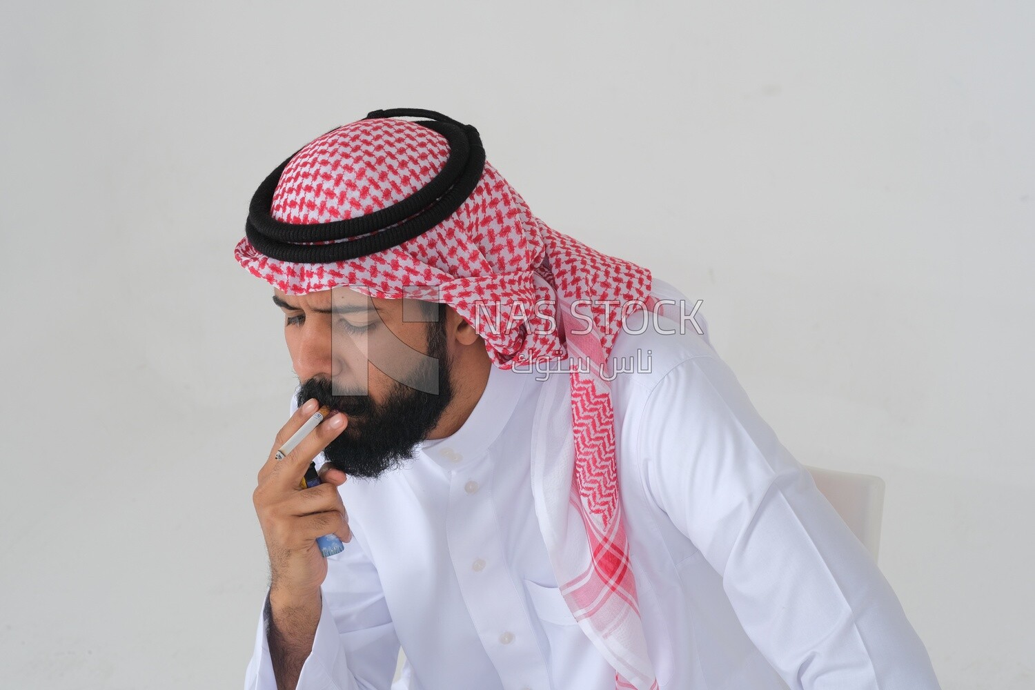 Saudi man wearing a white thobe and shemagh takes a deep breath from a cigarette, tobacco addiction, cigarette addiction, harmful and toxic substance abuse, harmful behavioral habits, no smoking, Saud
