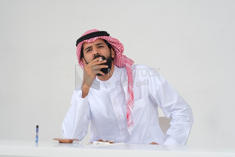 Saudi man wearing a white thobe and shemagh takes a deep breath from a cigarette