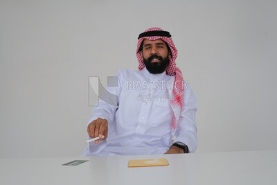 Saudi man wearing a white thobe and shemagh takes a deep breath from a cigarette, tobacco addiction, cigarette addiction, harmful and toxic substance abuse, harmful behavioral habits, no smoking, Saud